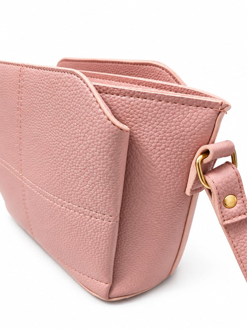 A close-up of a dusty pink pebbled leather shoulder bag with a matching strap and gold-tone hardware, set against a plain white background.