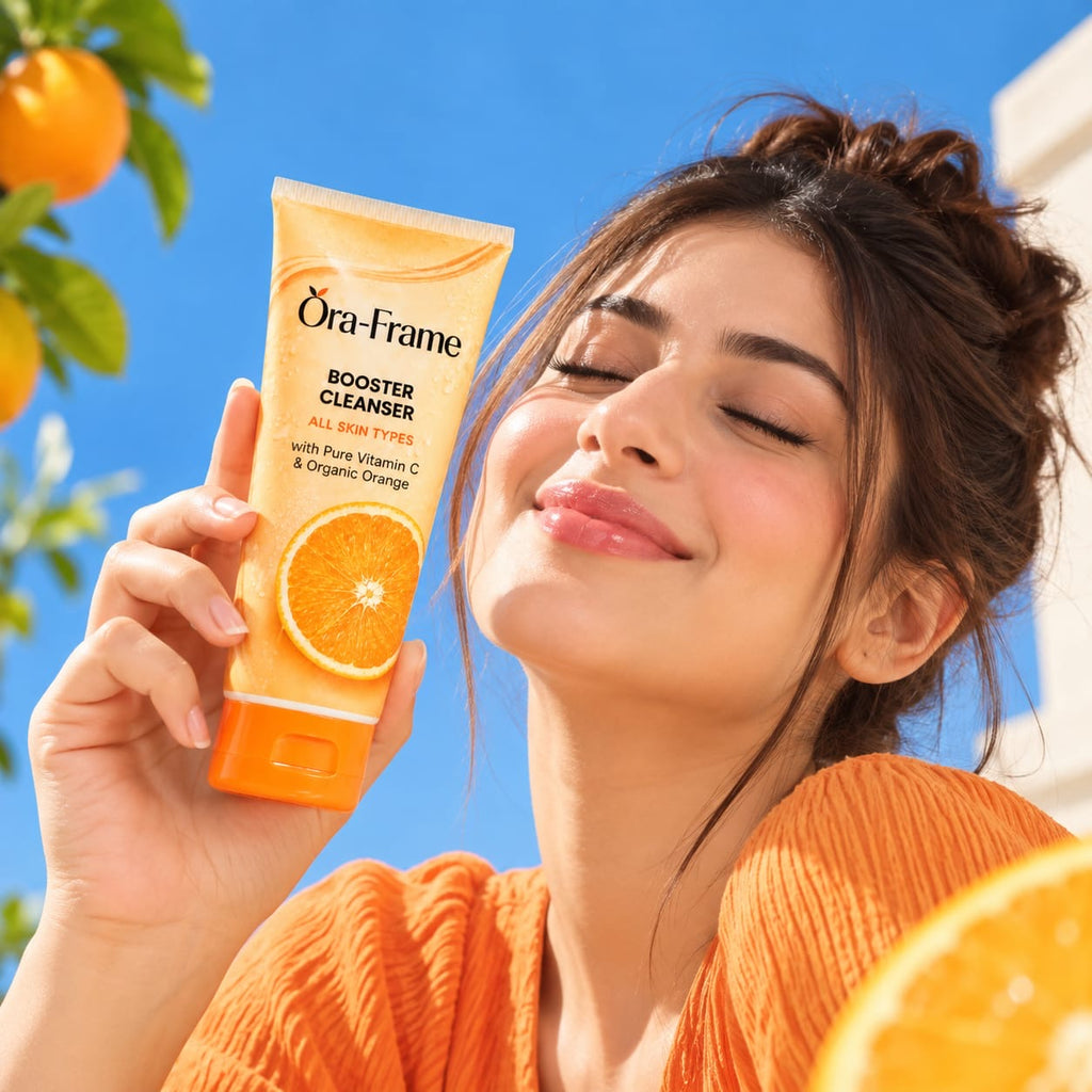 A woman outdoors holds up a tube of Öra-frame Booster Cleanser with orange graphics. The background features a bright blue sky, green leaves, and oranges.
